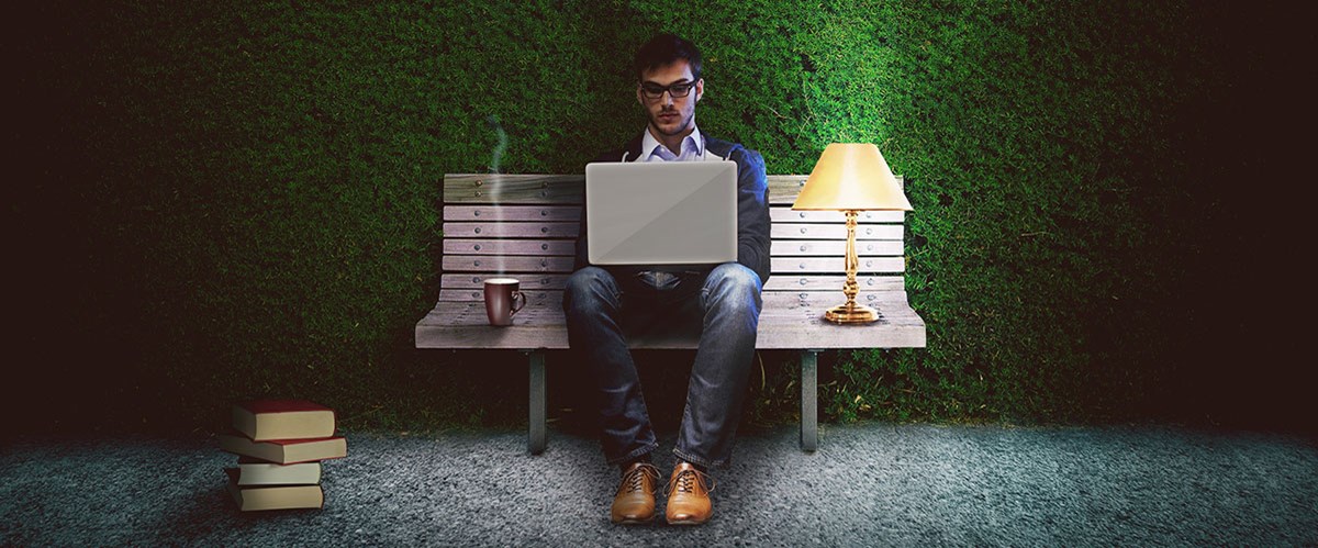 Mann som sitter på en benk med laptop i fanget